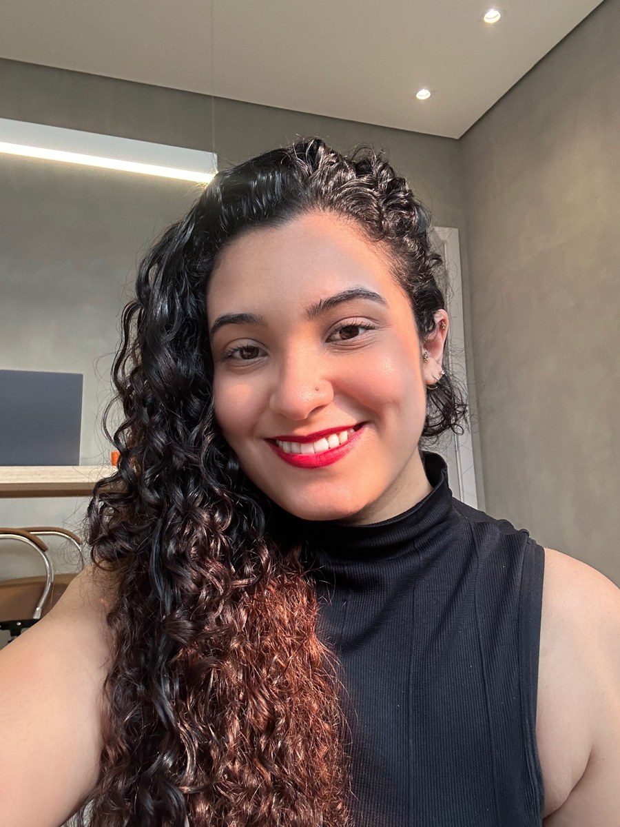 Luana Carolina sorrindo, de gola alta preta, no consultório.